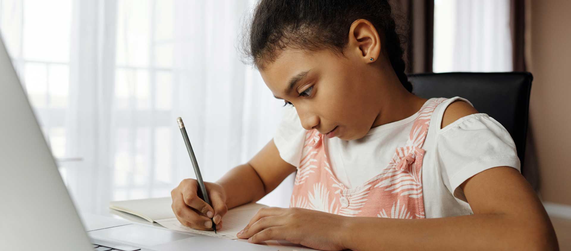 A school-age girl wrties at a desk in a home