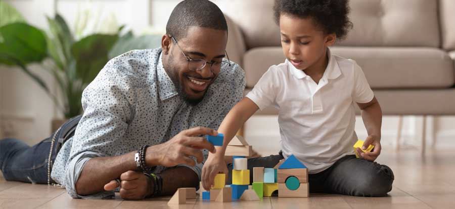 A smiling Black American father and child play with blocks on a living room floor
