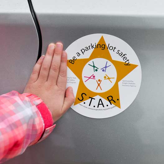 A young child's hand touches a vehicle next to a Star magnet