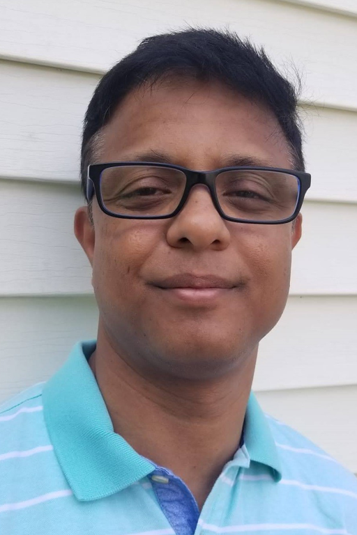 A man of south-Asian descent, with dark hair and wearing eye glasses and a blue striped polo shirt.