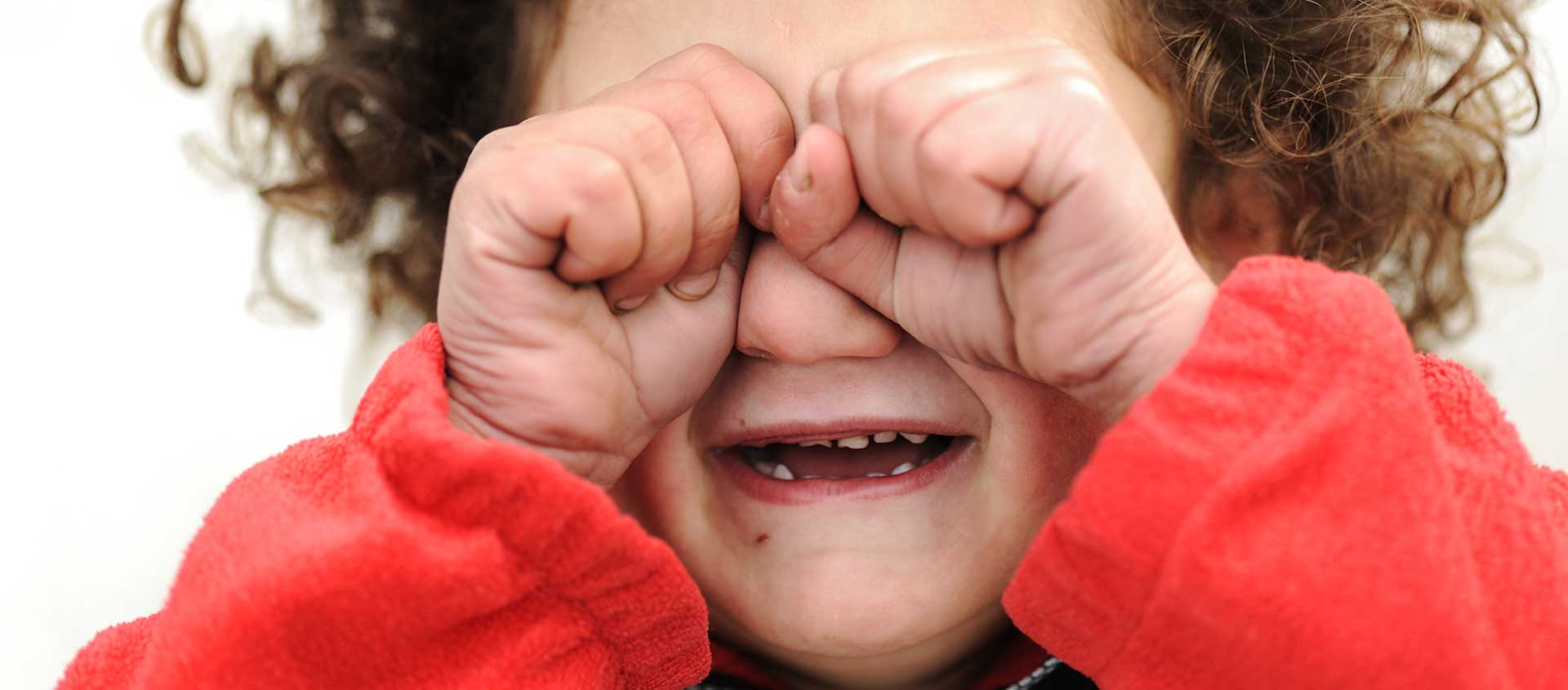 A preschool-aged child has his fists balled in his eyes and appears to be crying.