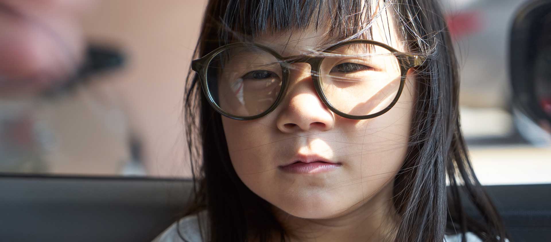 A young Asian girl wearing dark rimmed glasses sits at a table in a restaurant.