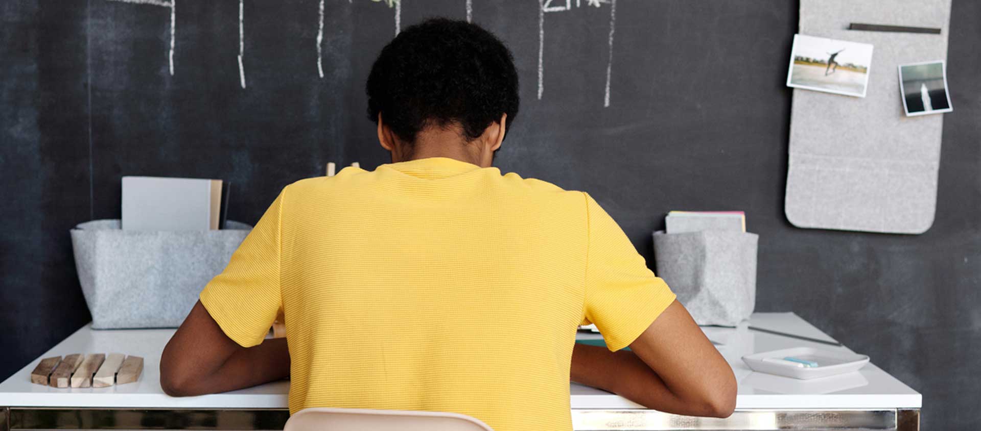 A Balck American boy studies at a desk with his back facing the camera.