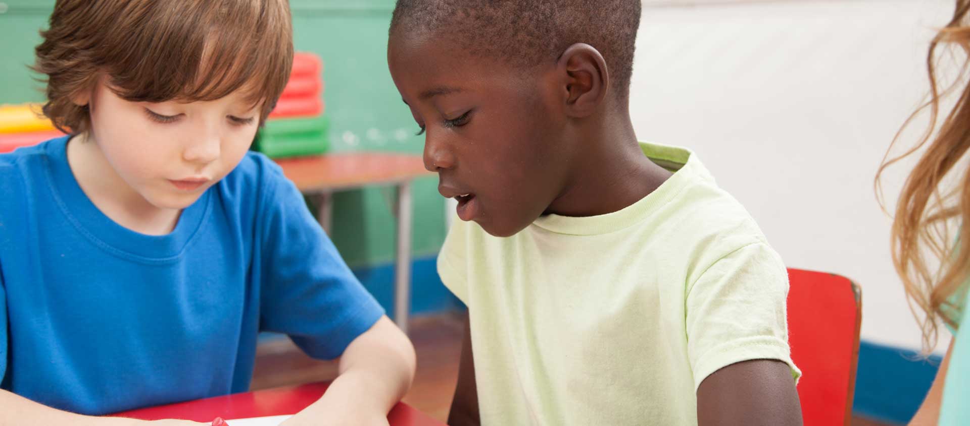 A Caucasian boy and a Black American boy are seated at a classroom table.