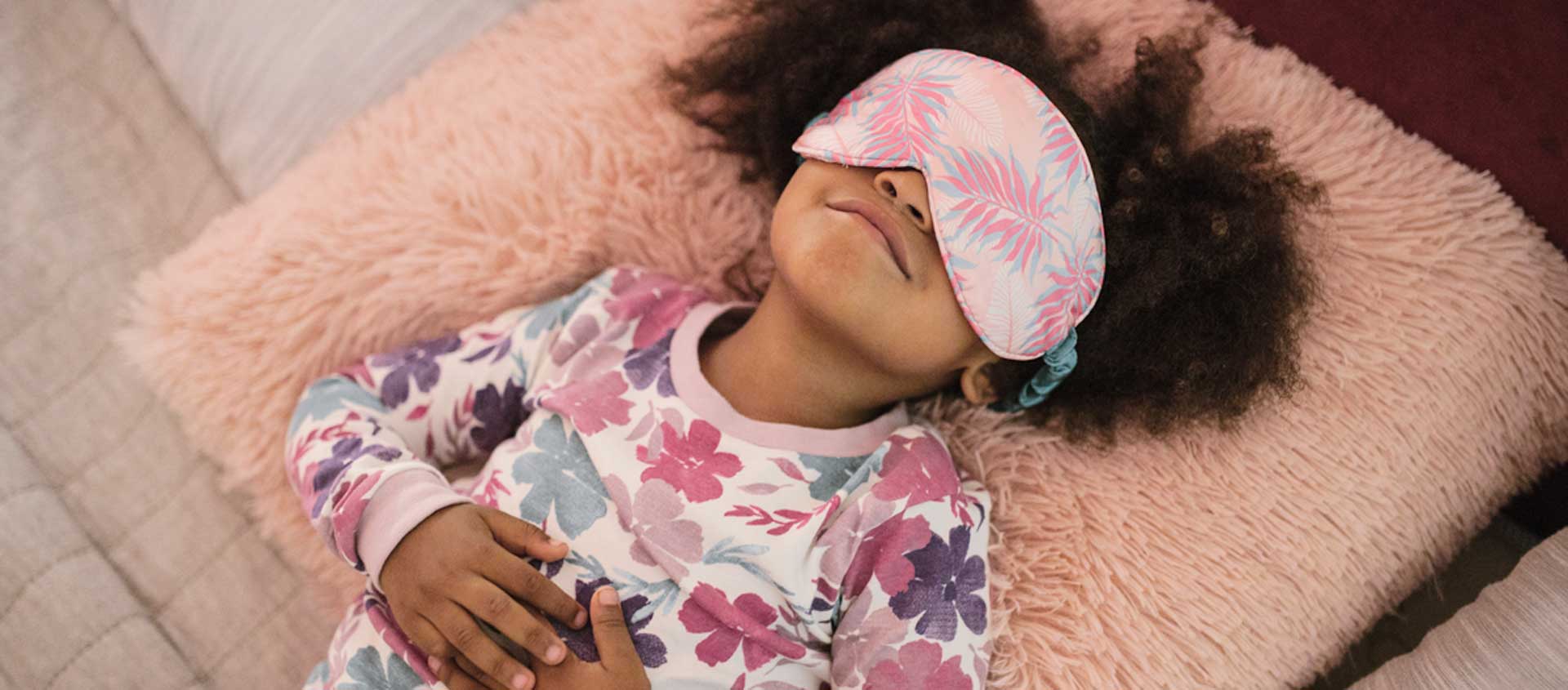 A Black American girl lays in bed with a sleep mask on.