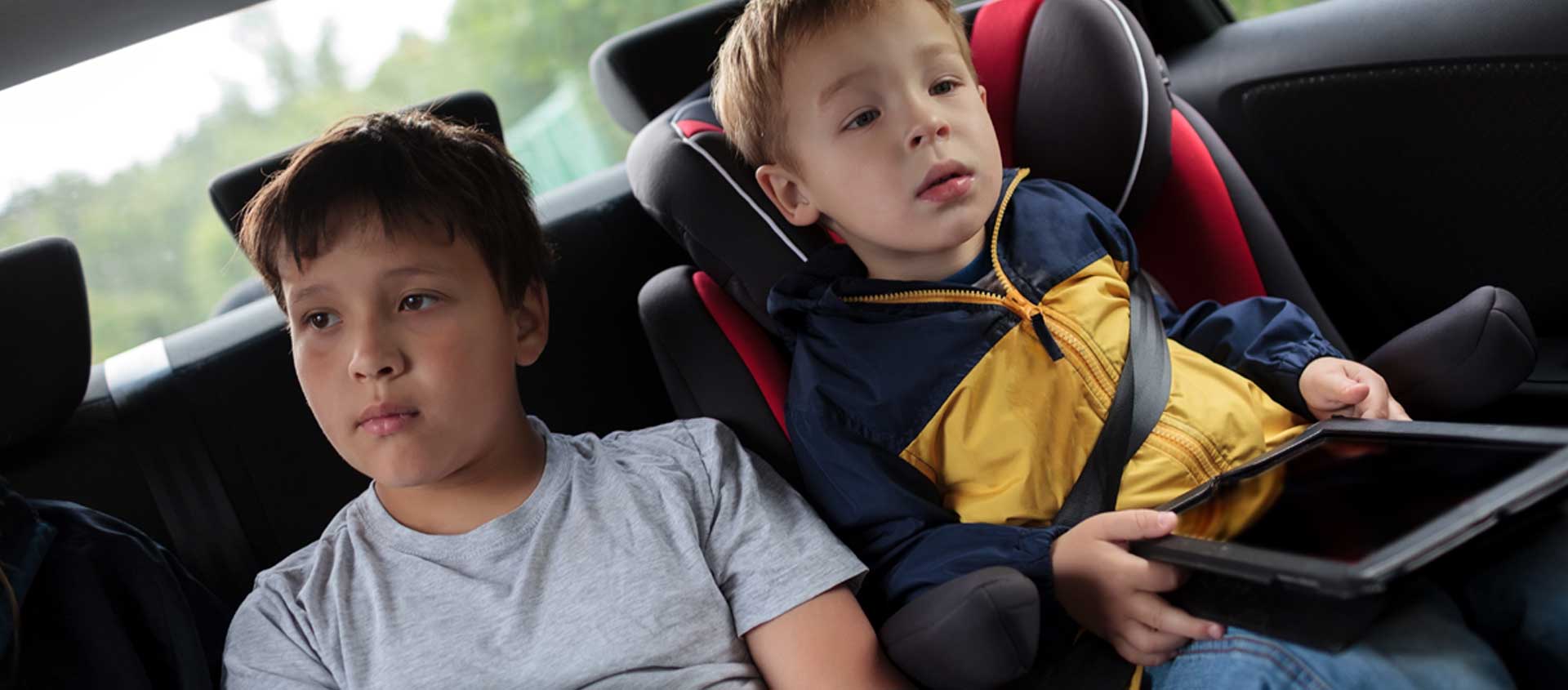 A school-age boy and his toddler brother sit in the back seat of the car.