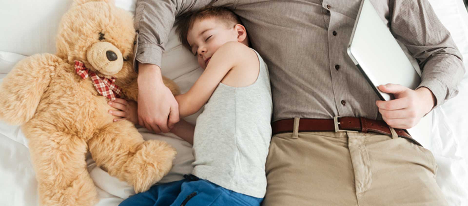 A child sleeps next to an adult in a bed.