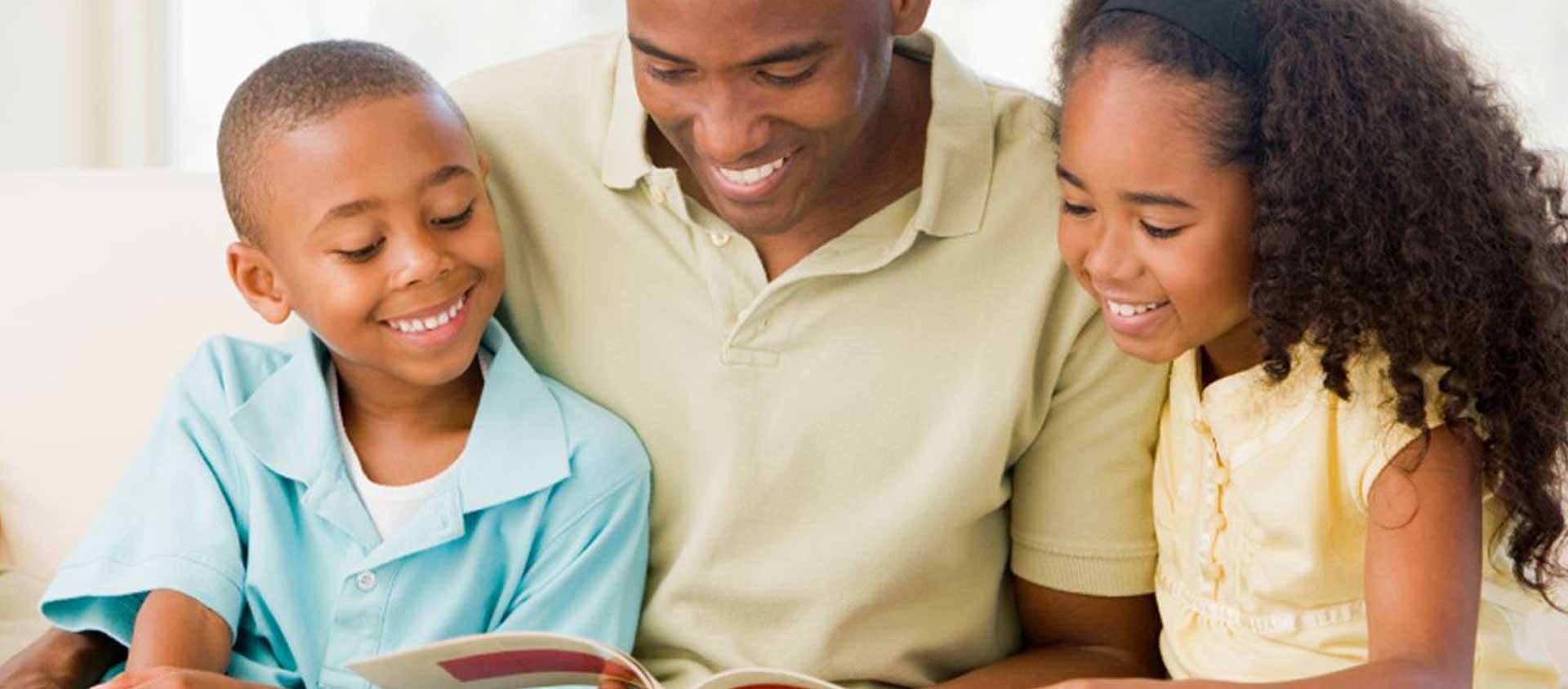 A Black American father reads a book to his children.