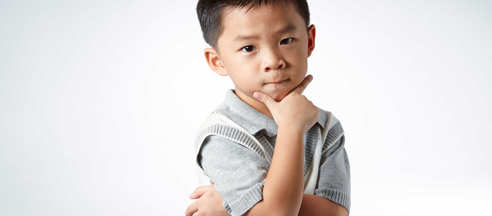 A preschool-aged Asian boy holds his head in one hand and looks on fiercely.