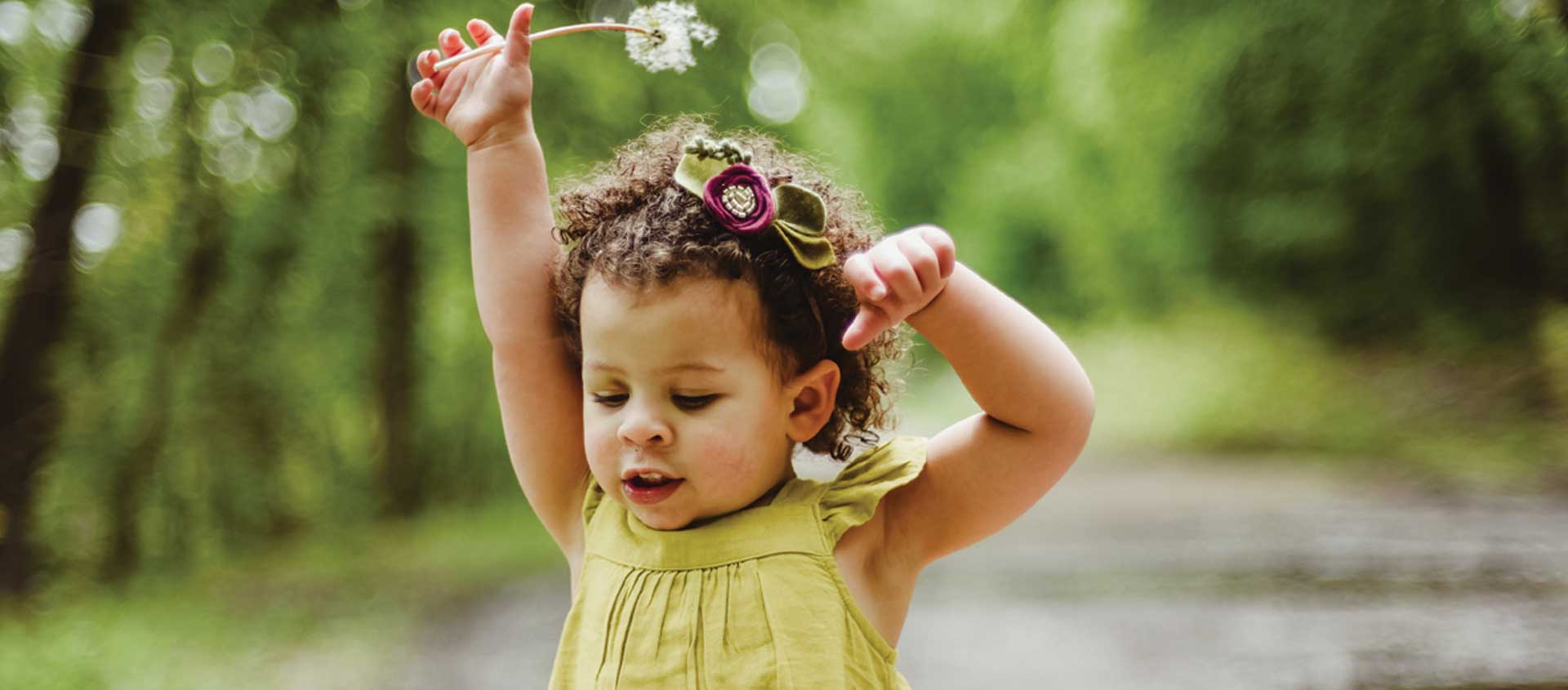 A toddler-age child with a dandelion in nature