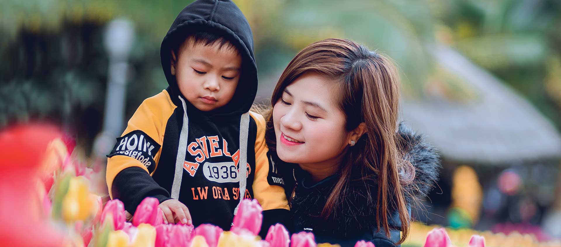 A mother and child of Asian descent look at a bed of tulips