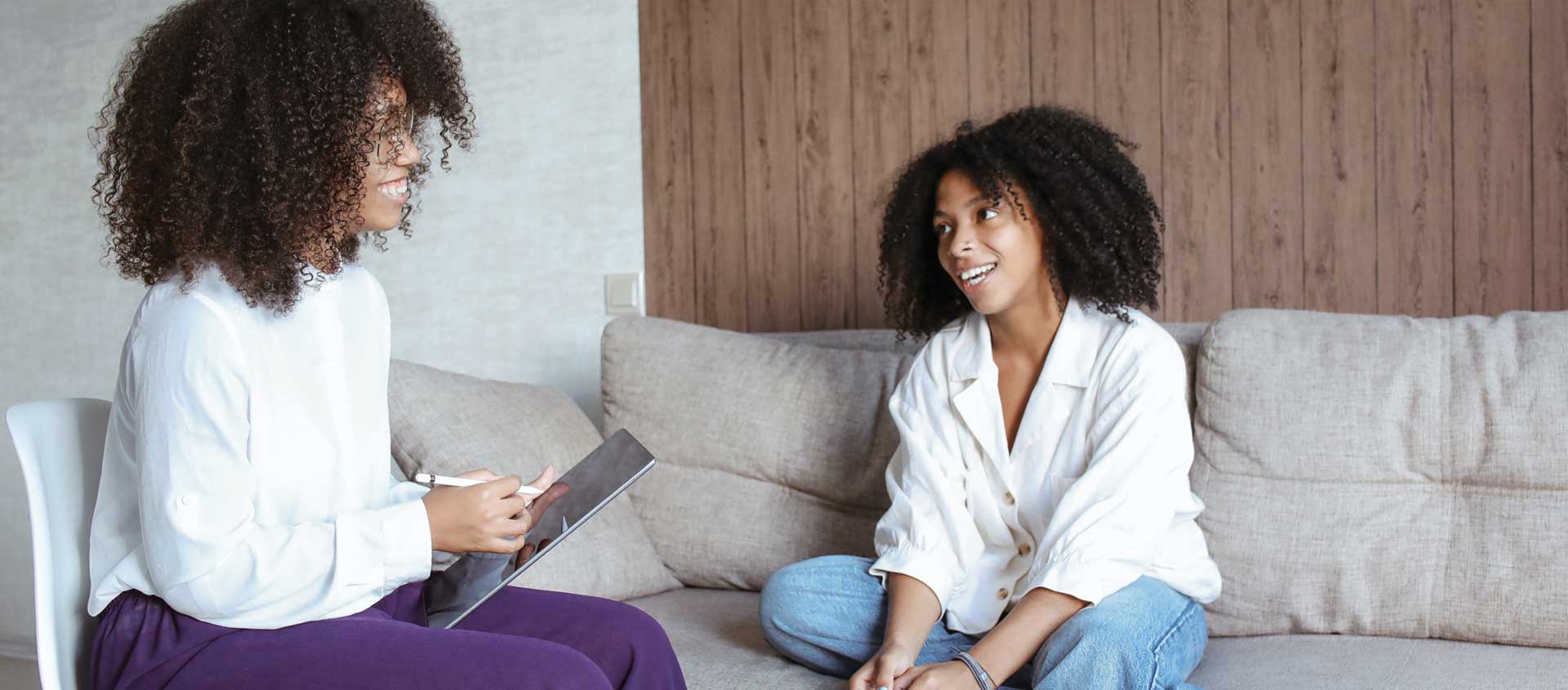 A Black American femal counselor sits on a couch with a pre-teen girl.