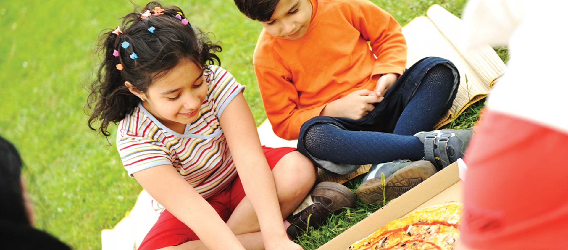 A borther and sister on a picnic sharing pizza.