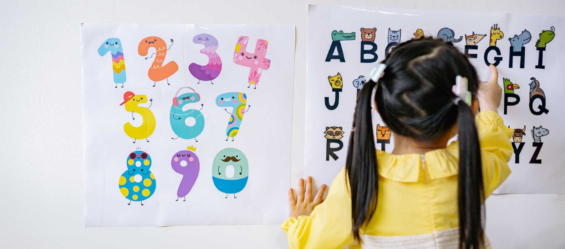 A dark-hared girl with pigtails points to letters on a poster.