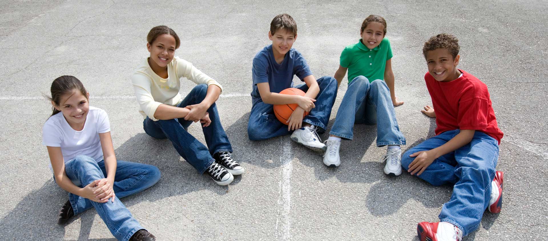 A group of tween firends sits together on a basketball court.