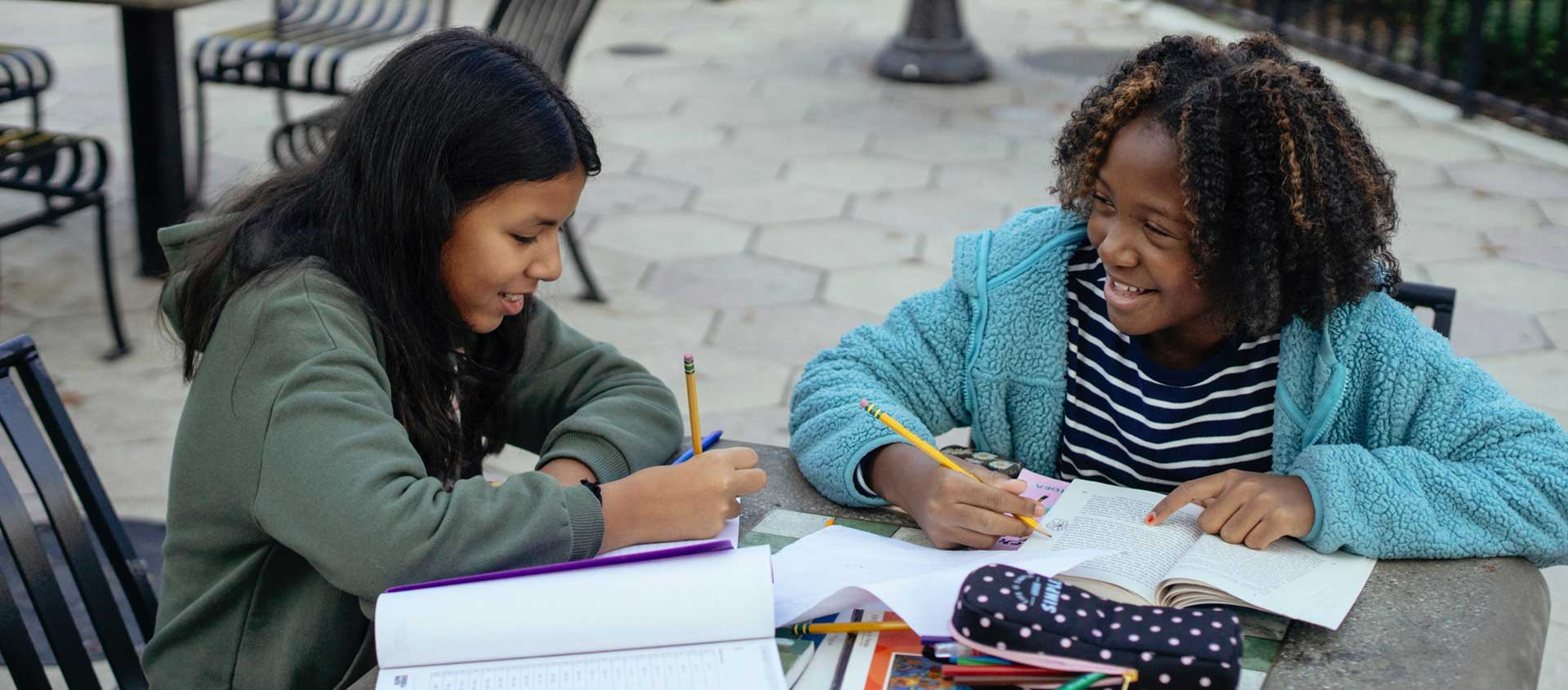 Two girls working on school work at an outdoor table. 